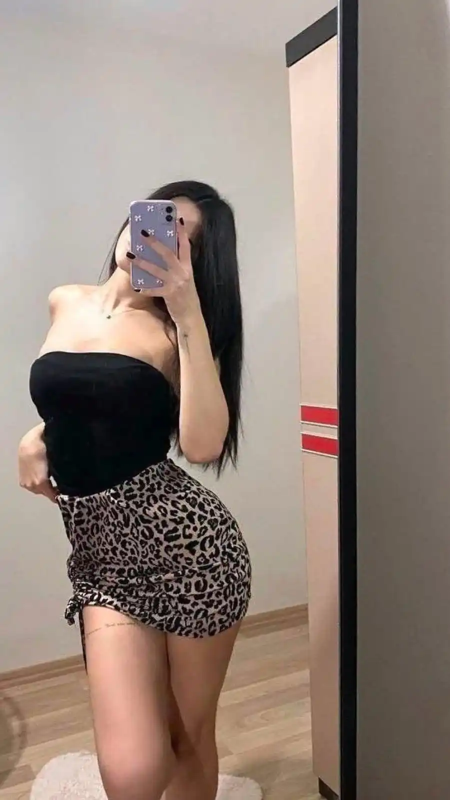 Person taking a mirror selfie wearing a strapless black top and a leopard-print mini skirt.