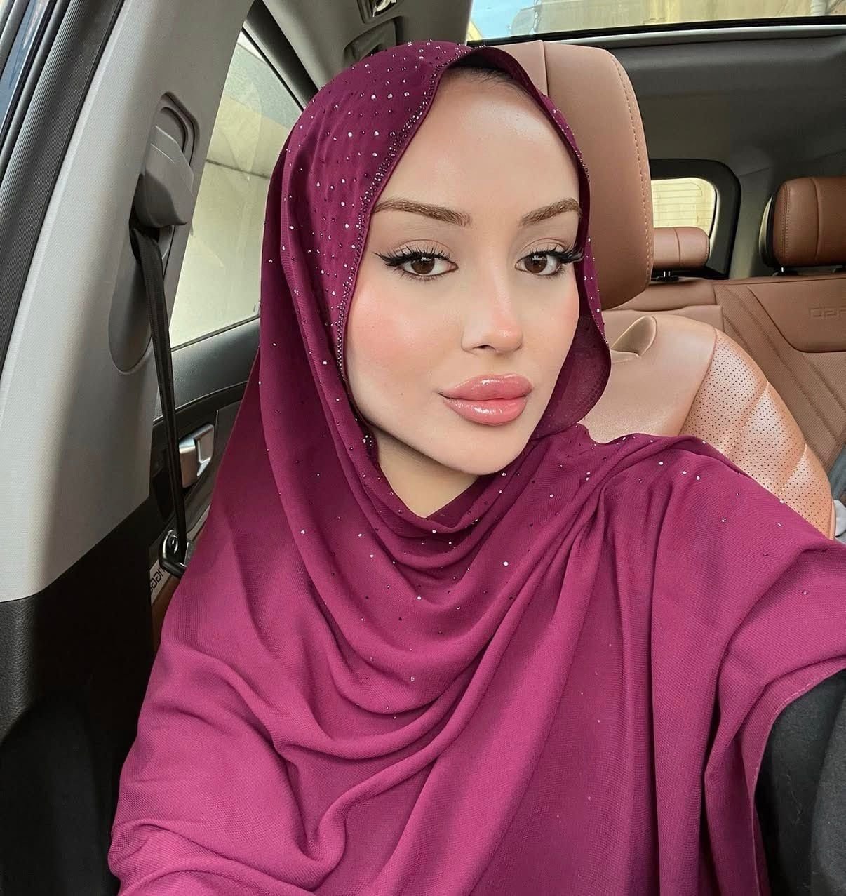 Close-up selfie of a woman in a sparkly magenta hijab inside a car with tan leather seats.
