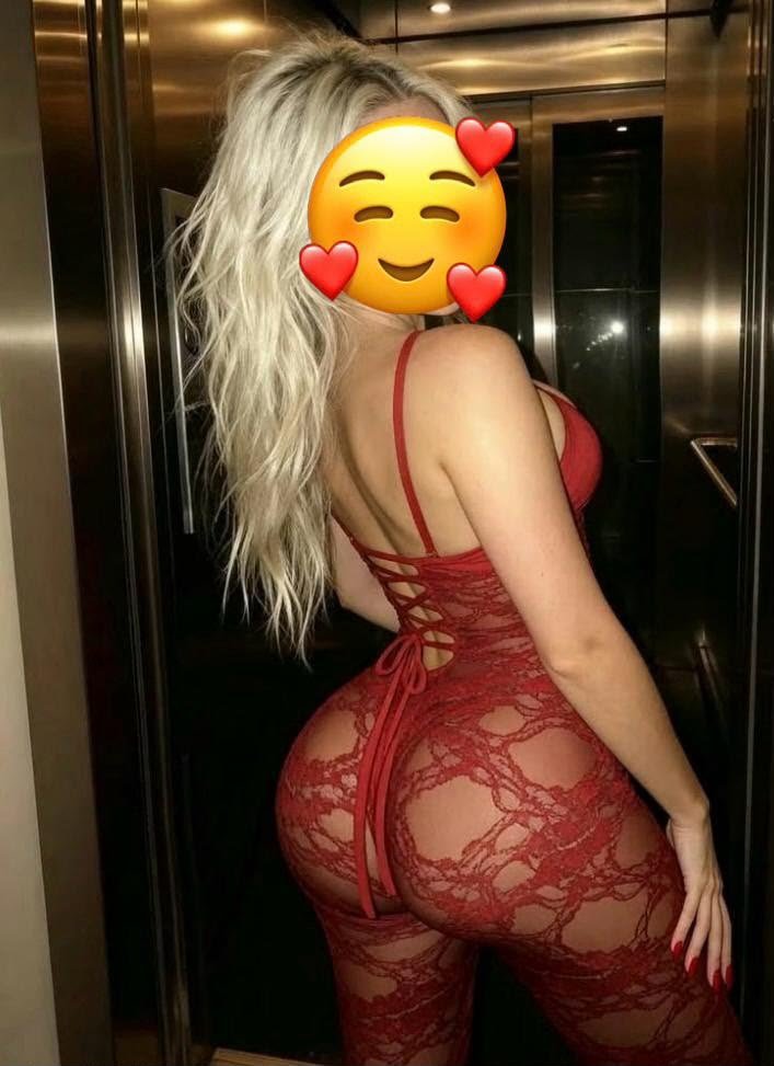 Back view of a person in a red lace bodysuit posing in an elevator, face obscured by an emoji sticker.